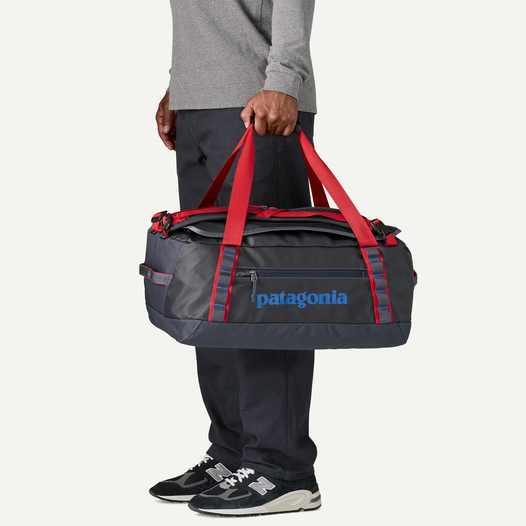Person carrying Patagonia Black Hole Duffel bag in smolder blue with red straps