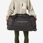 Person holding Patagonia Black Hole Wheeled Duffel 70L in black with wheels visible