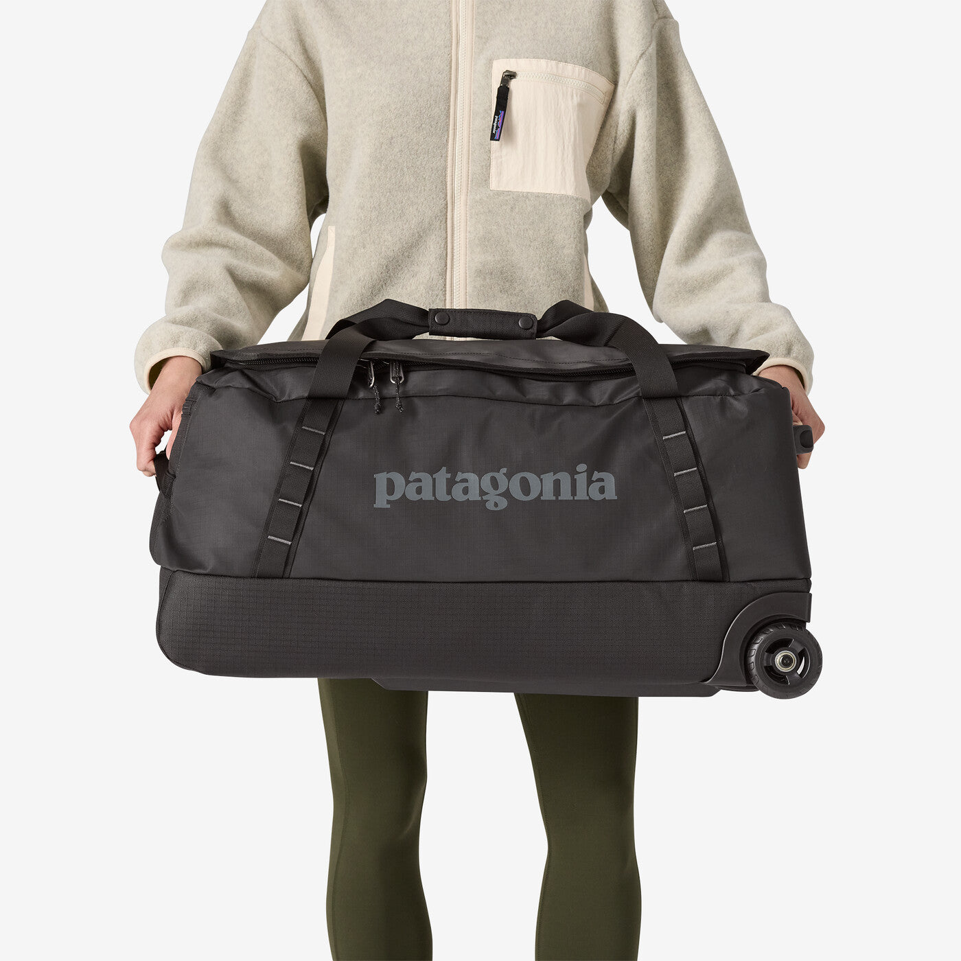 Person holding Patagonia Black Hole Wheeled Duffel 70L in black with wheels visible