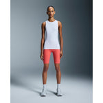 Woman wearing white sleeveless tank top and coral shorts in studio setting