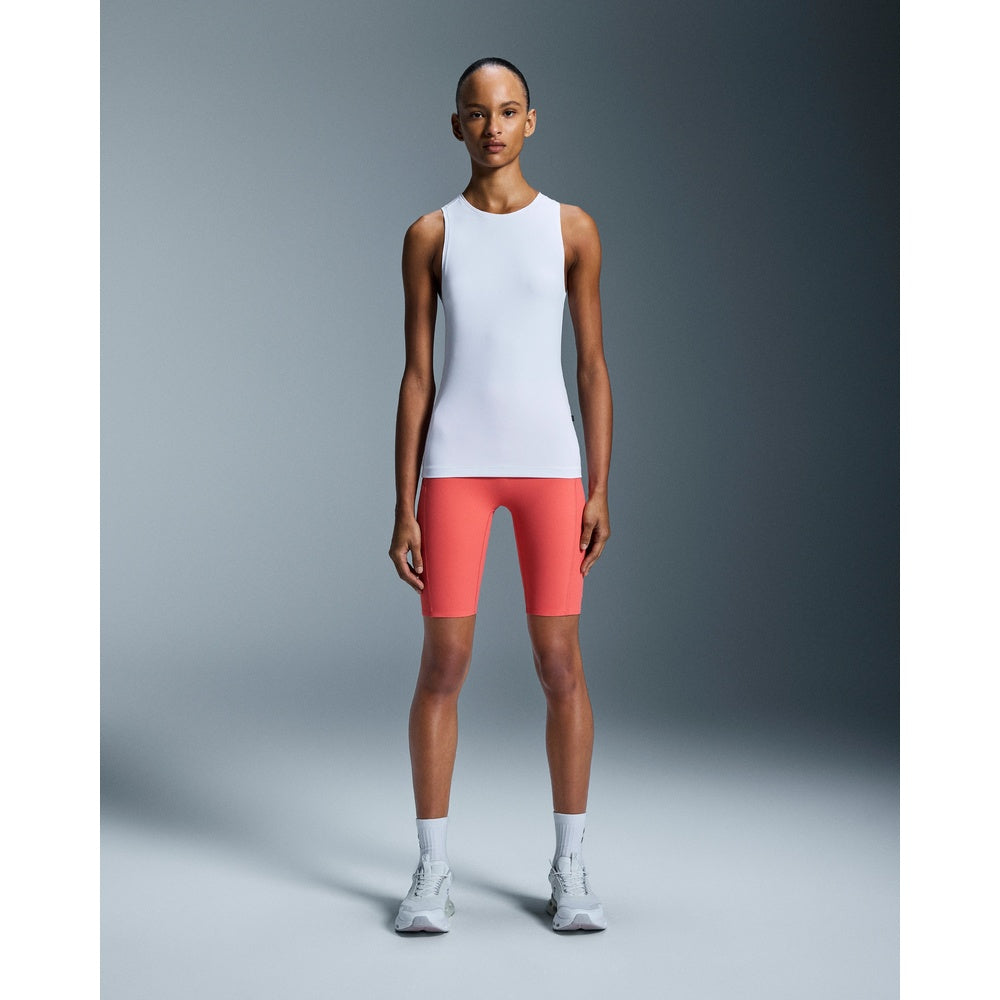 Woman wearing white sleeveless tank top and coral shorts in studio setting