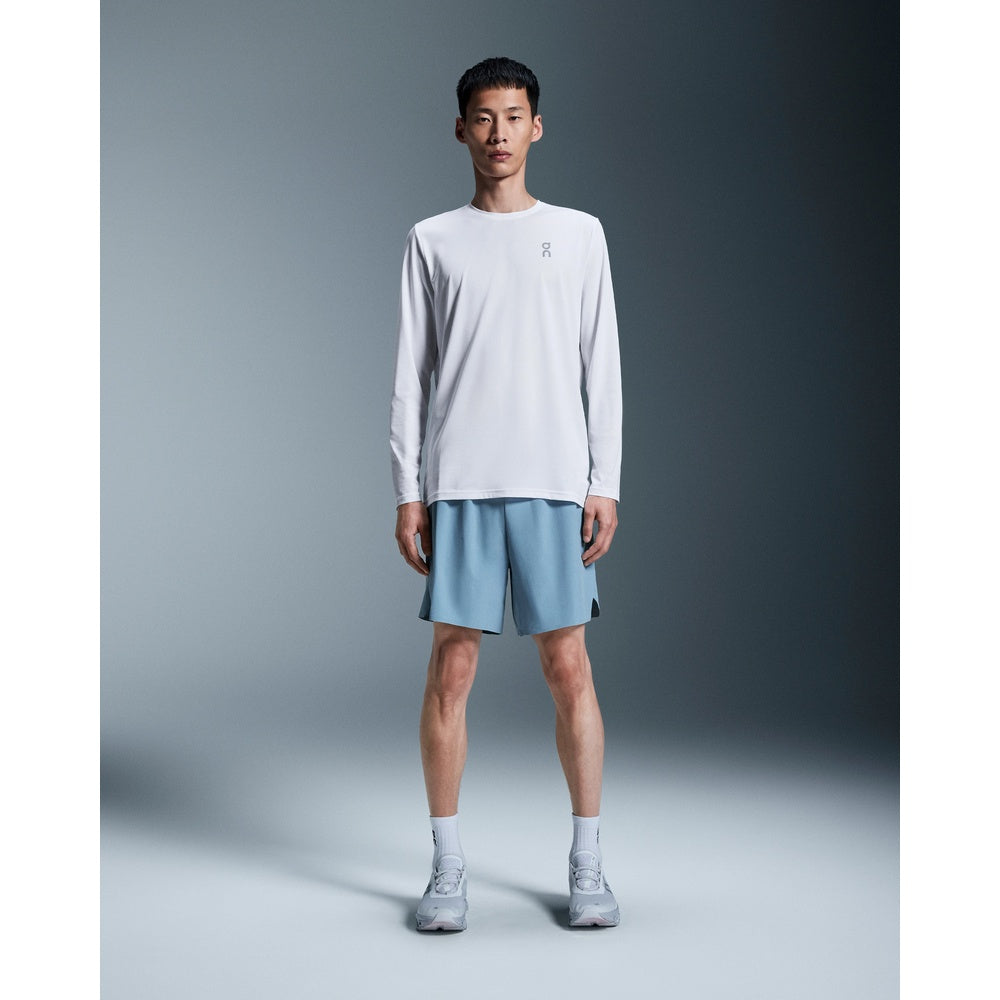 Man wearing white On Core Long-T shirt with blue shorts in studio setting