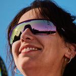 Woman wearing Goodr Tentacle Tag Champion sunglasses with purple frame and rainbow mirrored lenses