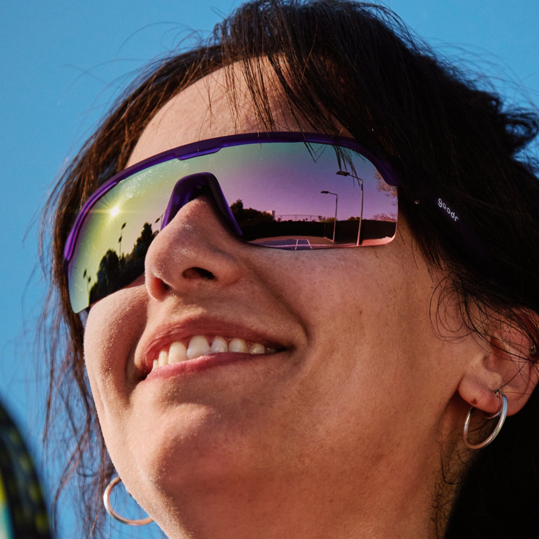 Woman wearing Goodr Tentacle Tag Champion sunglasses with purple frame and rainbow mirrored lenses
