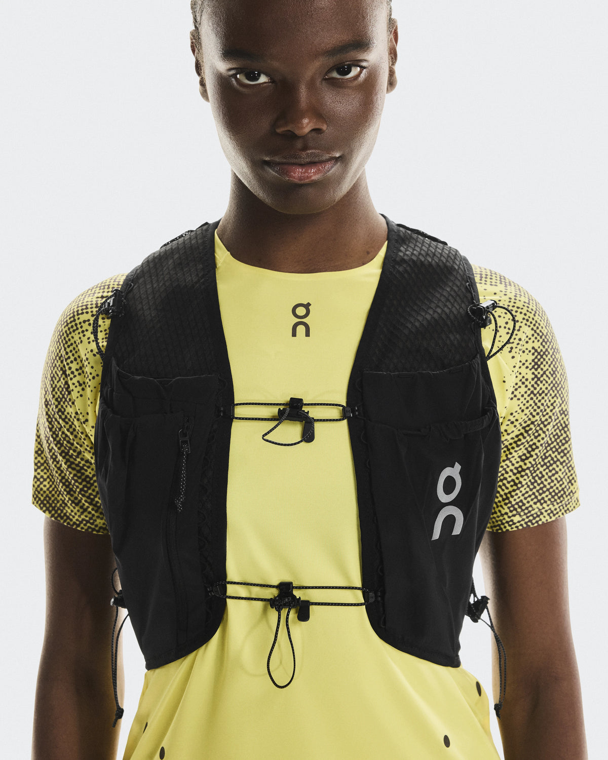 On Ultra Vest Pro Unisex in black worn over yellow On running shirt, front view