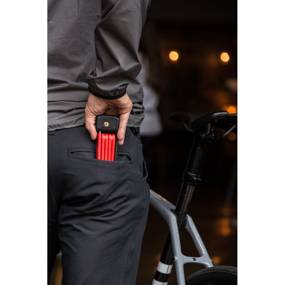 Person holding red Abus Bordo folding bike lock next to bicycle