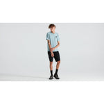 Man wearing light blue Specialized S-logo t-shirt with black shorts in studio setting