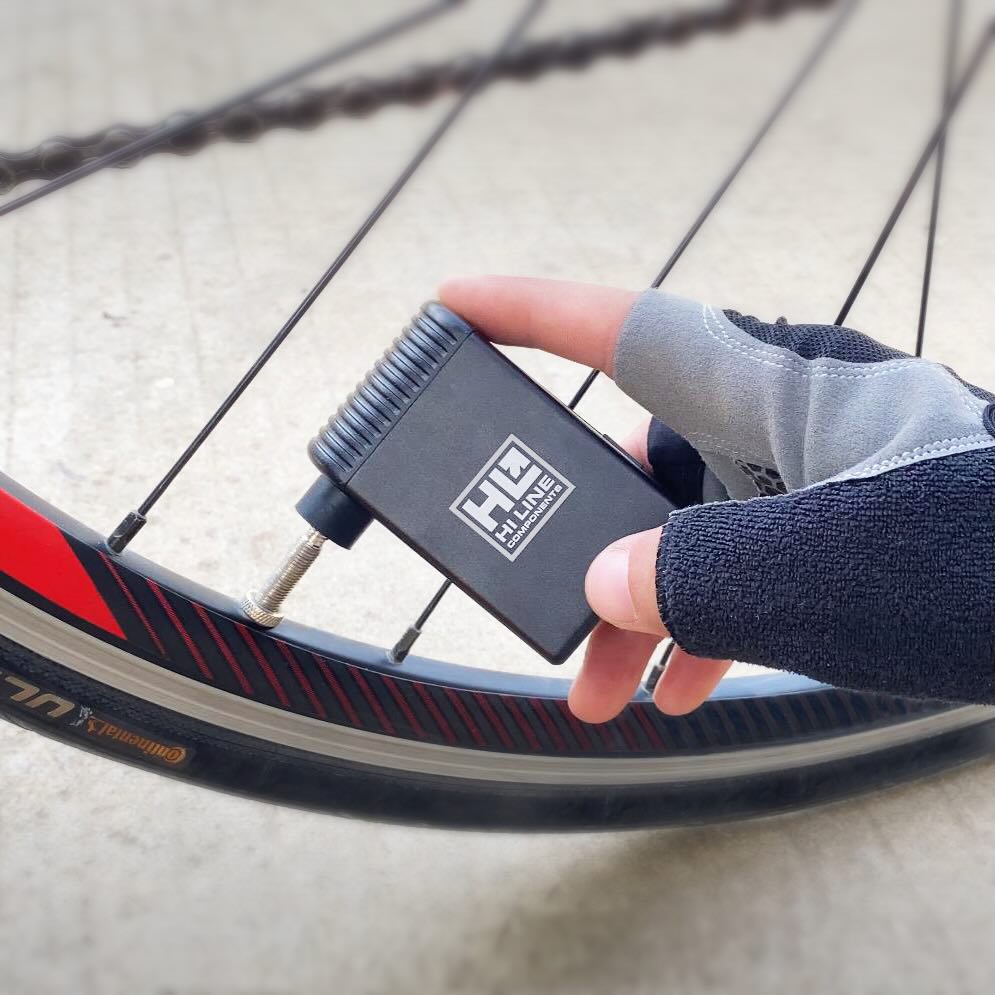 Hand holding black Hi-Line electric tire pump next to bicycle wheel