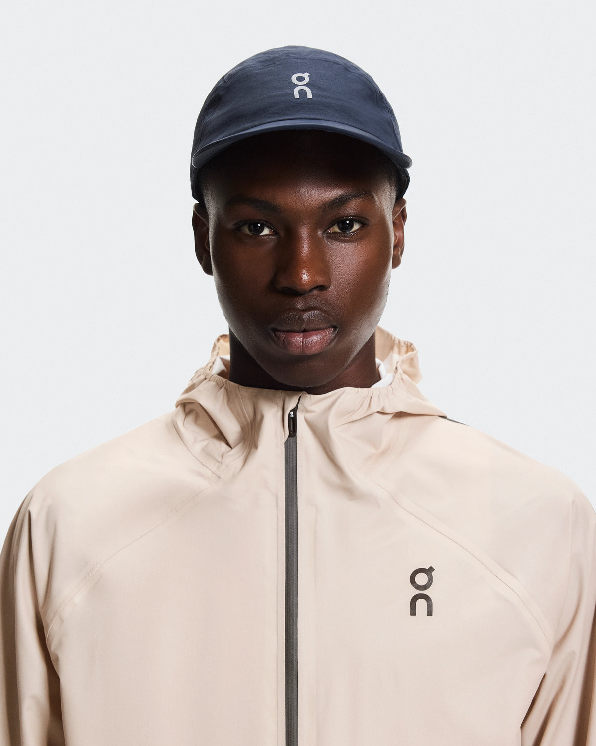 Model wearing On Performance Cap in navy blue with matching On hooded jacket
