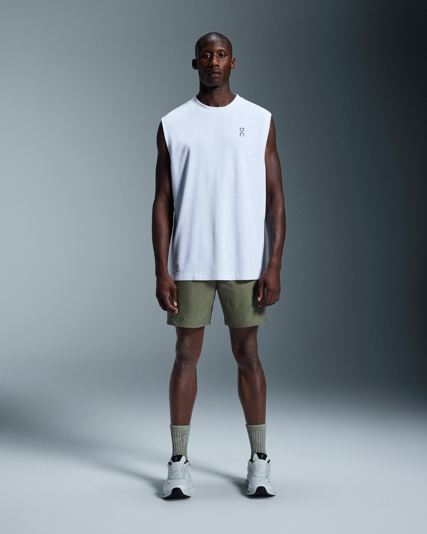 Man wearing On 7 inch Core Shorts in taiga green with white sleeveless shirt