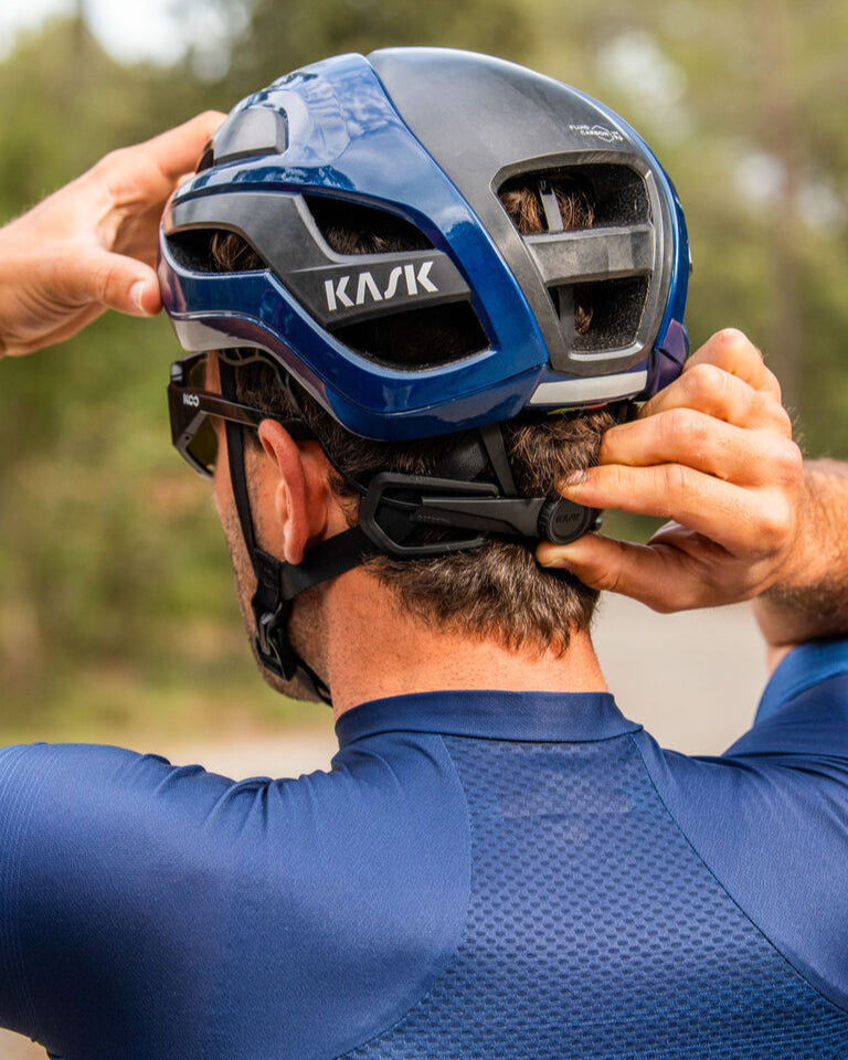 Person adjusting blue and silver Kask Elemento cycling helmet outdoors
