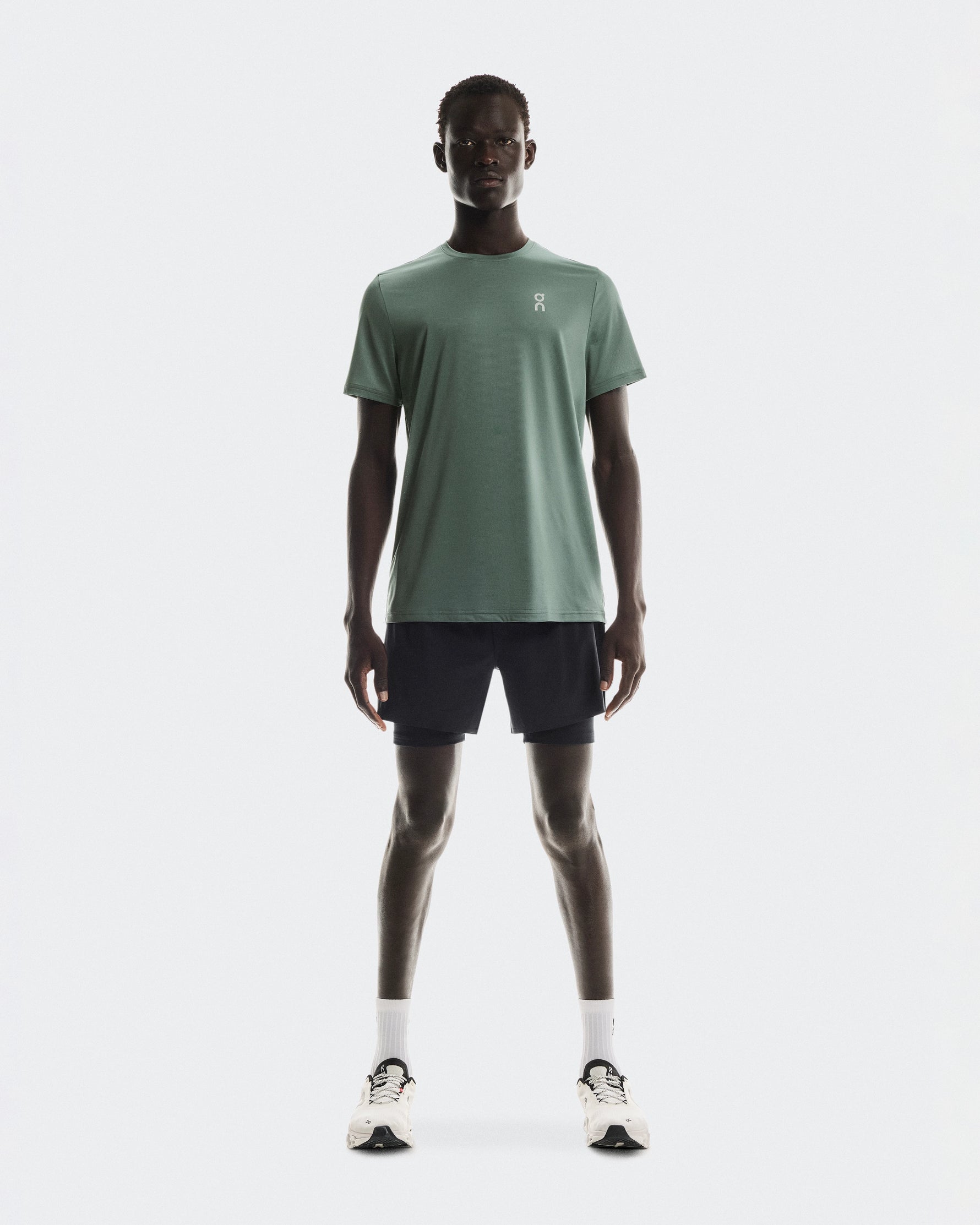 Man wearing On Core-T shirt in sage green with black shorts and white sneakers