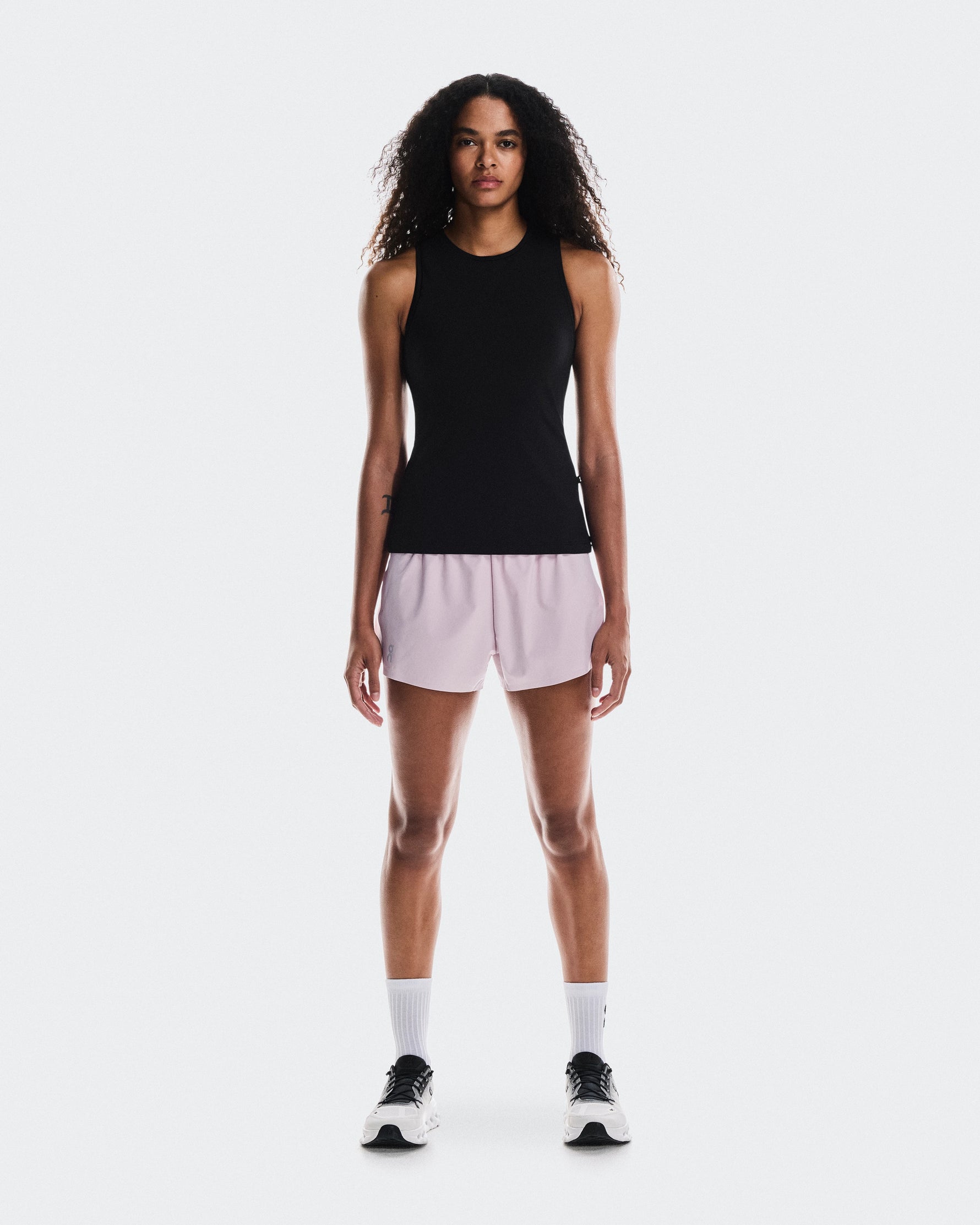 Woman wearing black sleeveless tank top with light pink shorts and white sneakers