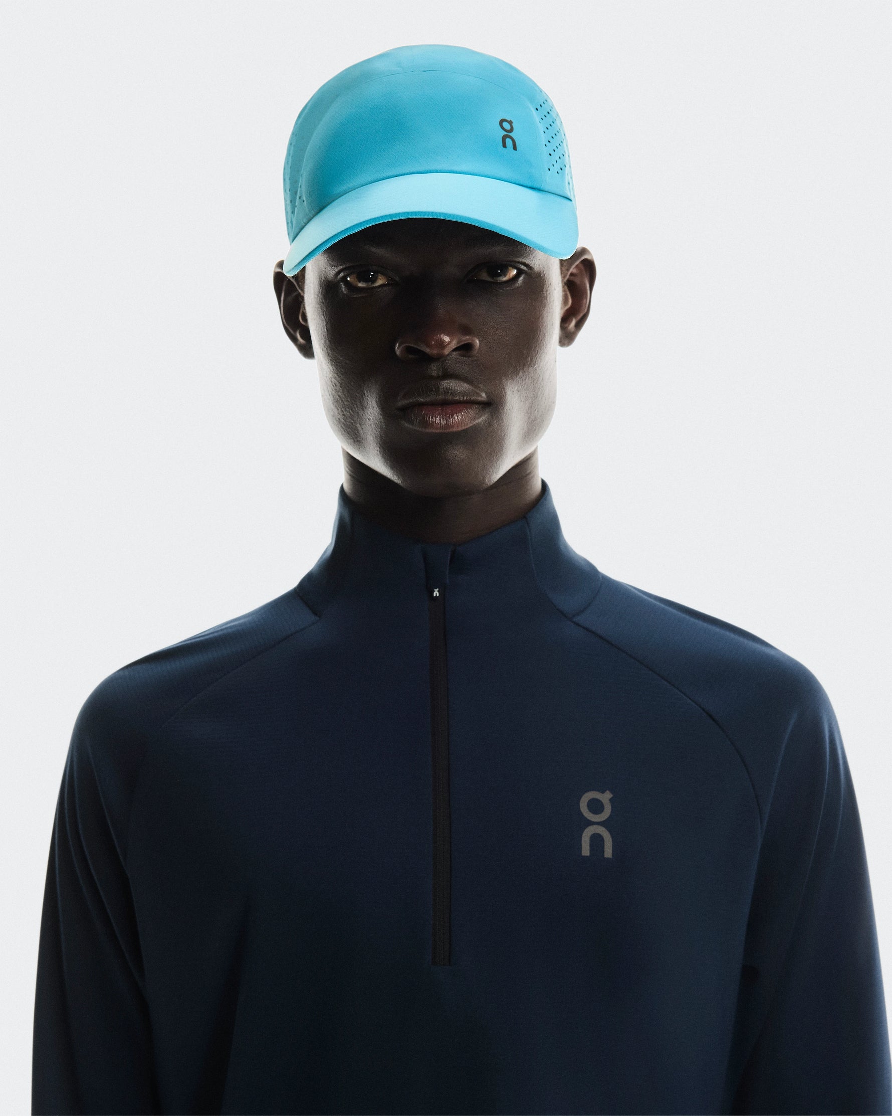 Model wearing light blue On Lightweight Unisex Cap with navy running jacket