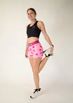 Woman wearing pink heart-patterned compression shorts with black sports top in studio setting