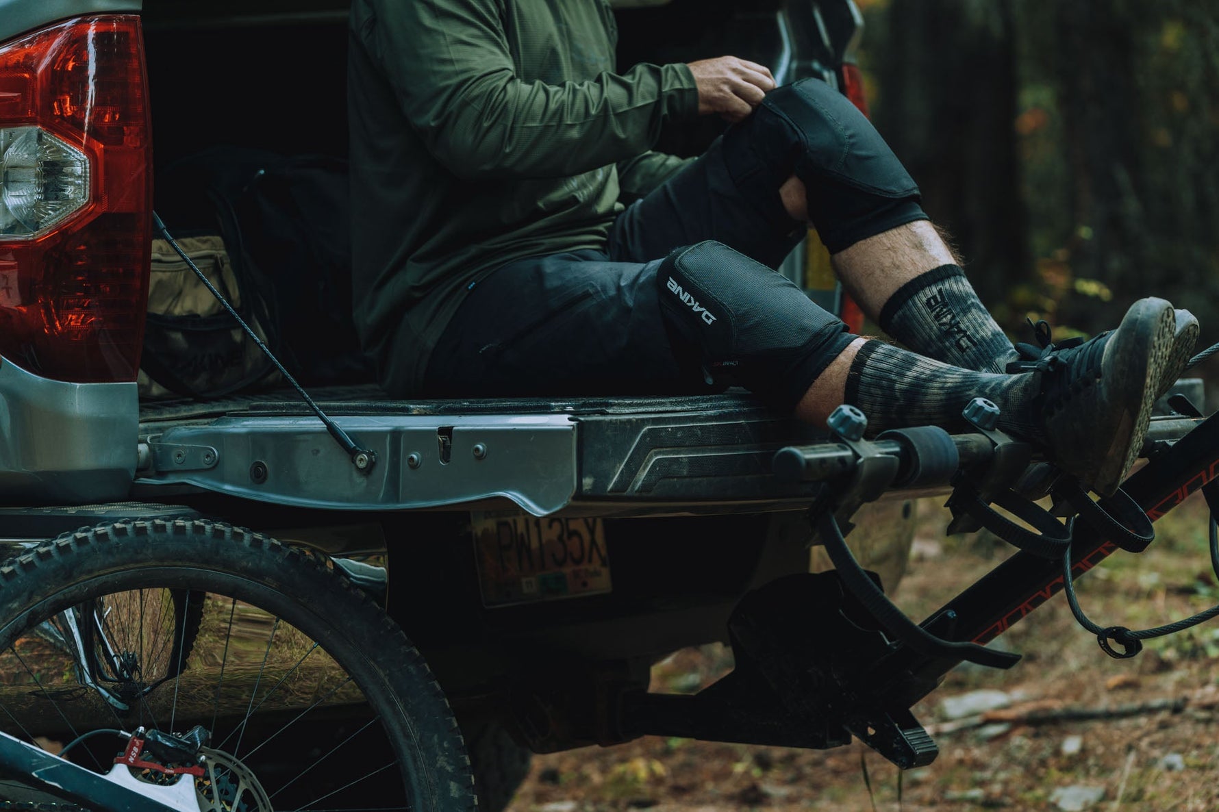 Person wearing black Dakine knee pads while sitting on truck tailgate with mountain bike
