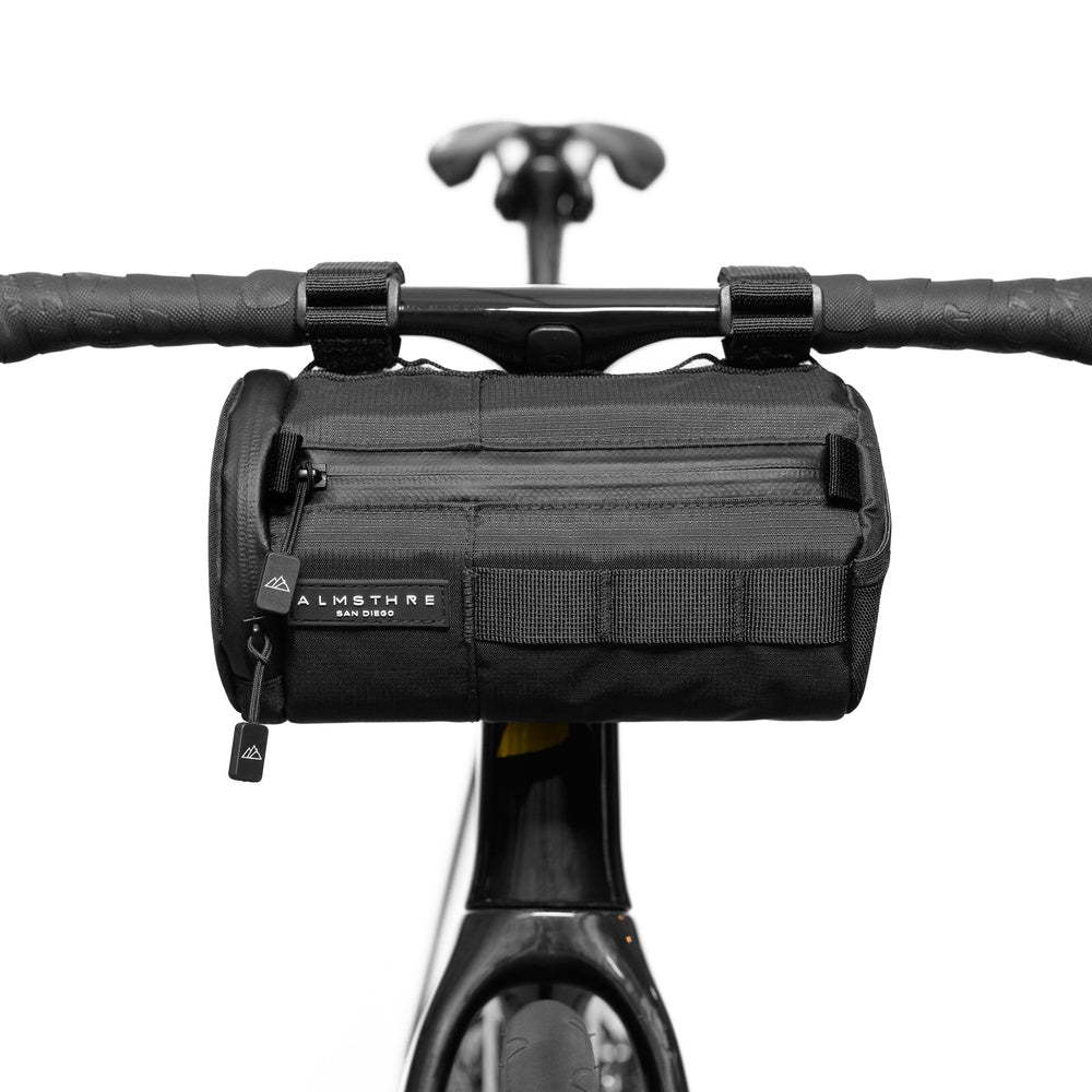 Black ALMSTHRE bicycle handlebar bag mounted on bike handlebars against white background