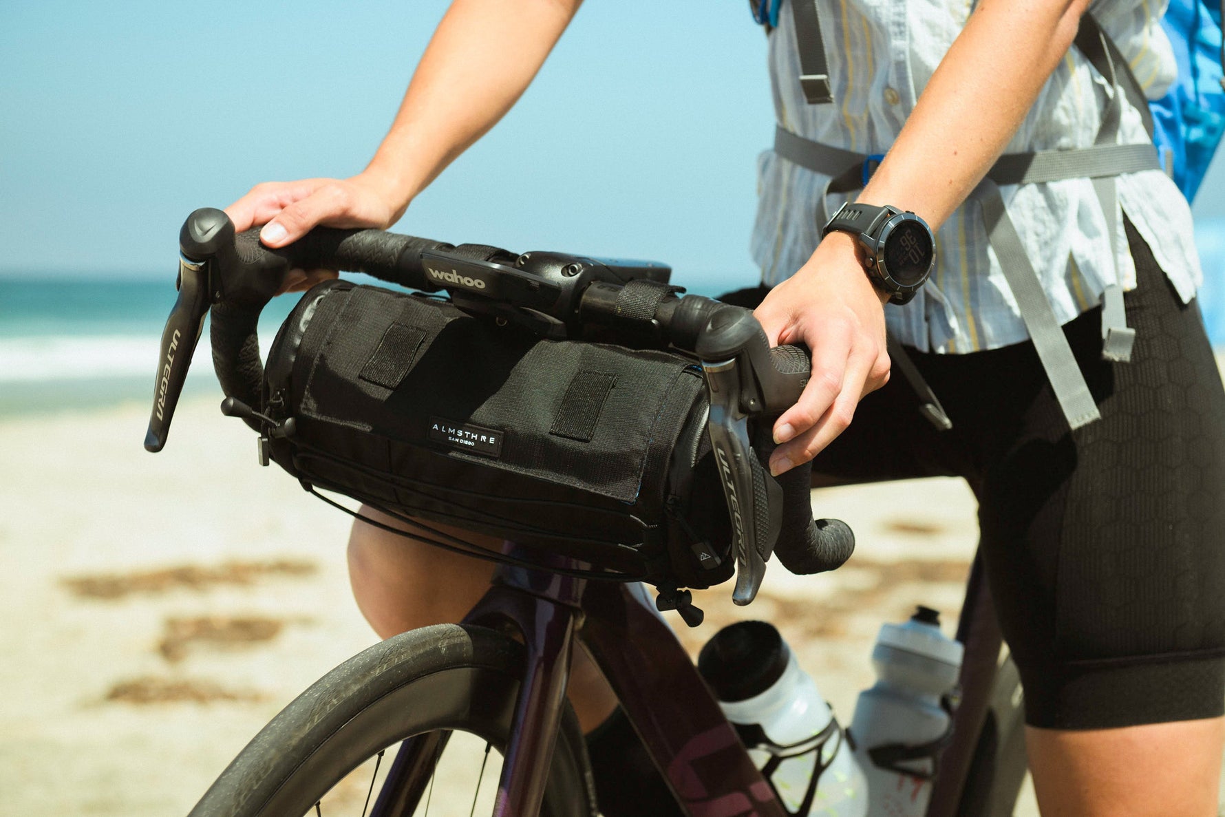 Person with ALMSTHRE black bicycle handlebar bag mounted on bike at beach