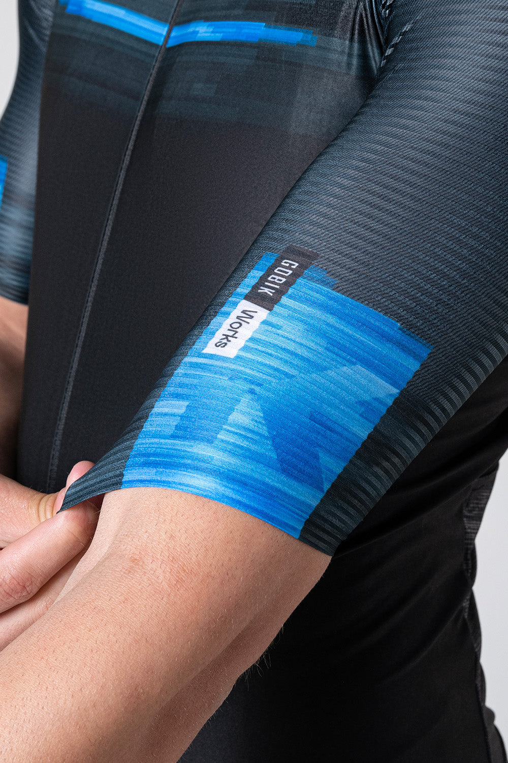 Gobik cycling jersey sleeve detail showing black fabric with blue gradient pattern and logo