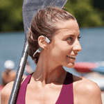 Woman wearing white AfterShokz bone conduction headphones while holding tennis racket outdoors