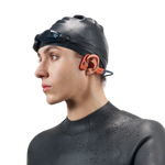 Person wearing orange Shokz bone conduction headphones with swim cap and goggles