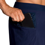 Man placing phone in zippered pocket of navy Brooks Sherpa running shorts