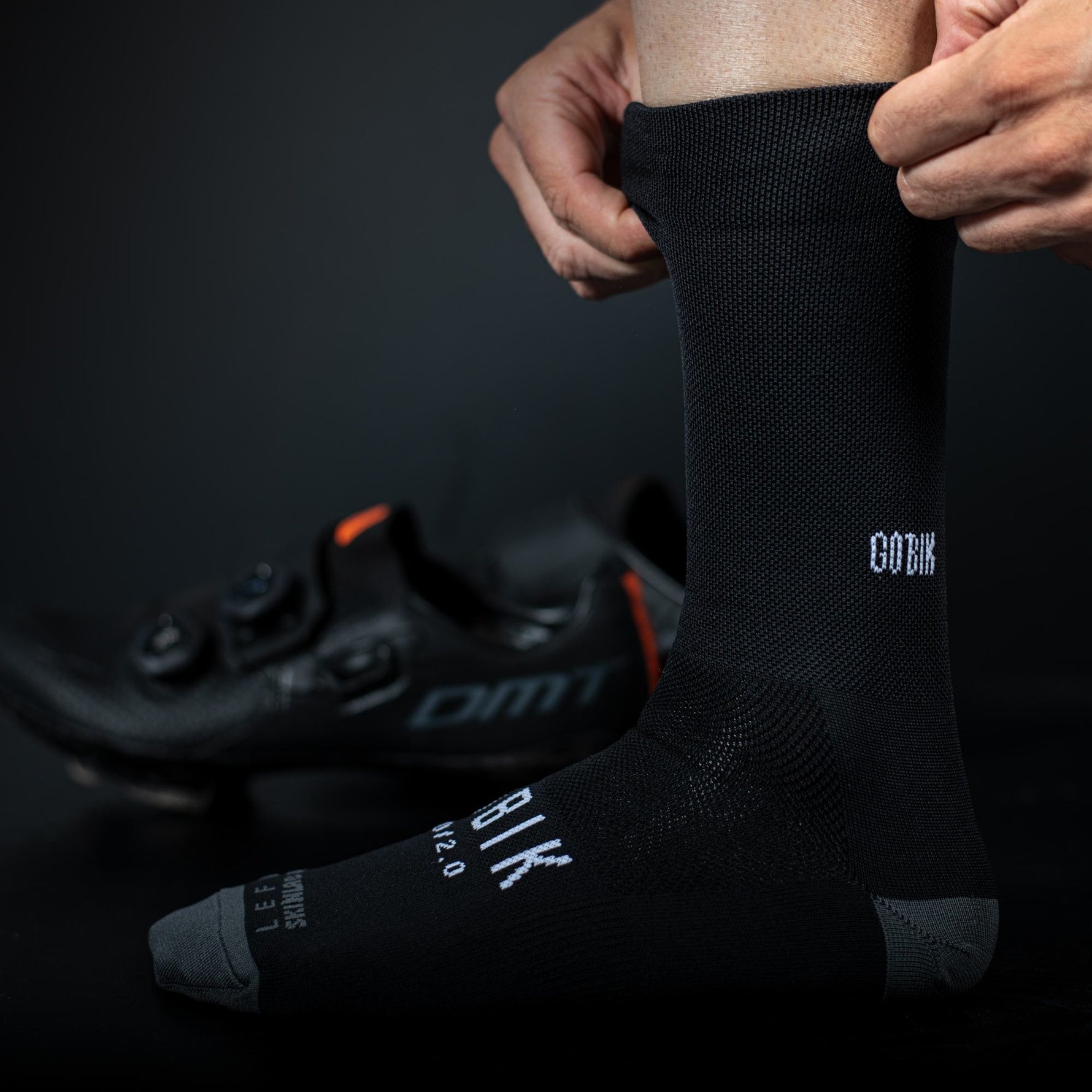 Person putting on black Gobik cycling socks with white logo branding
