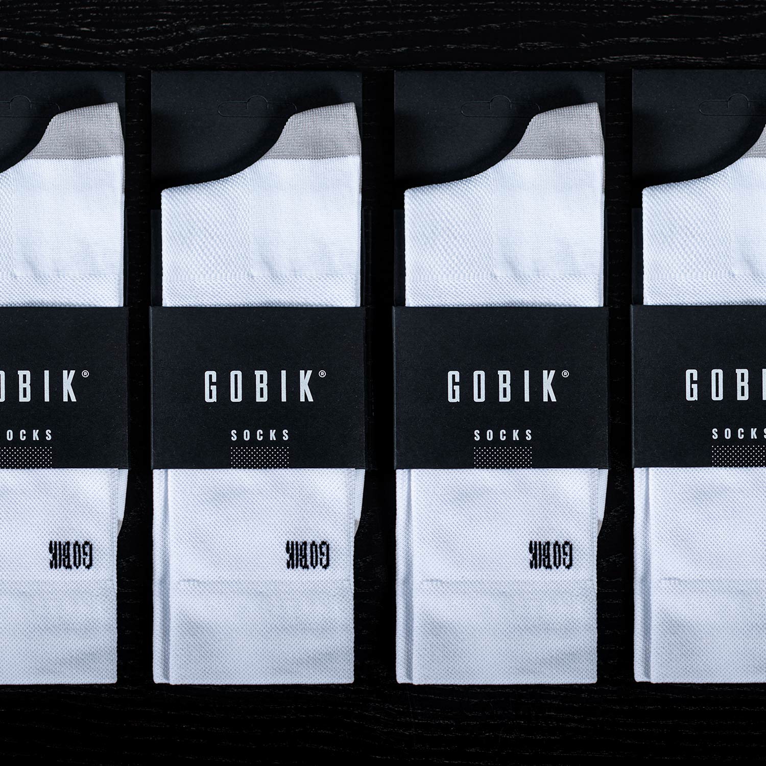 Four packages of white Gobik socks with black branding in product packaging