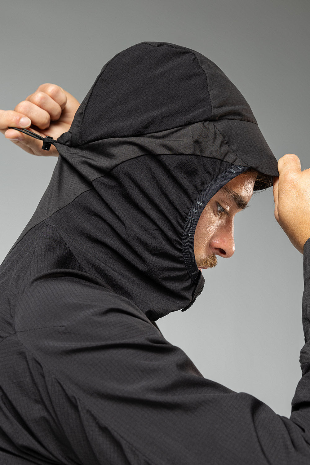 Man wearing black Gobik lightweight rain jacket with hood up adjusting hood drawstring