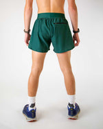 Man wearing forest green athletic running shorts with split hem, back view
