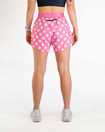 Woman wearing pink polka dot athletic shorts with white sneakers on clean background