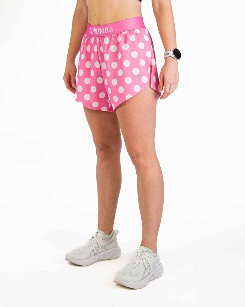 Woman wearing pink polka dot athletic shorts with white sneakers on clean background