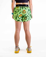 Woman wearing green pickle-patterned athletic shorts with black waistband, back view