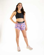 Woman wearing purple ChicknLegs split shorts with pink pig pattern and black sports bra