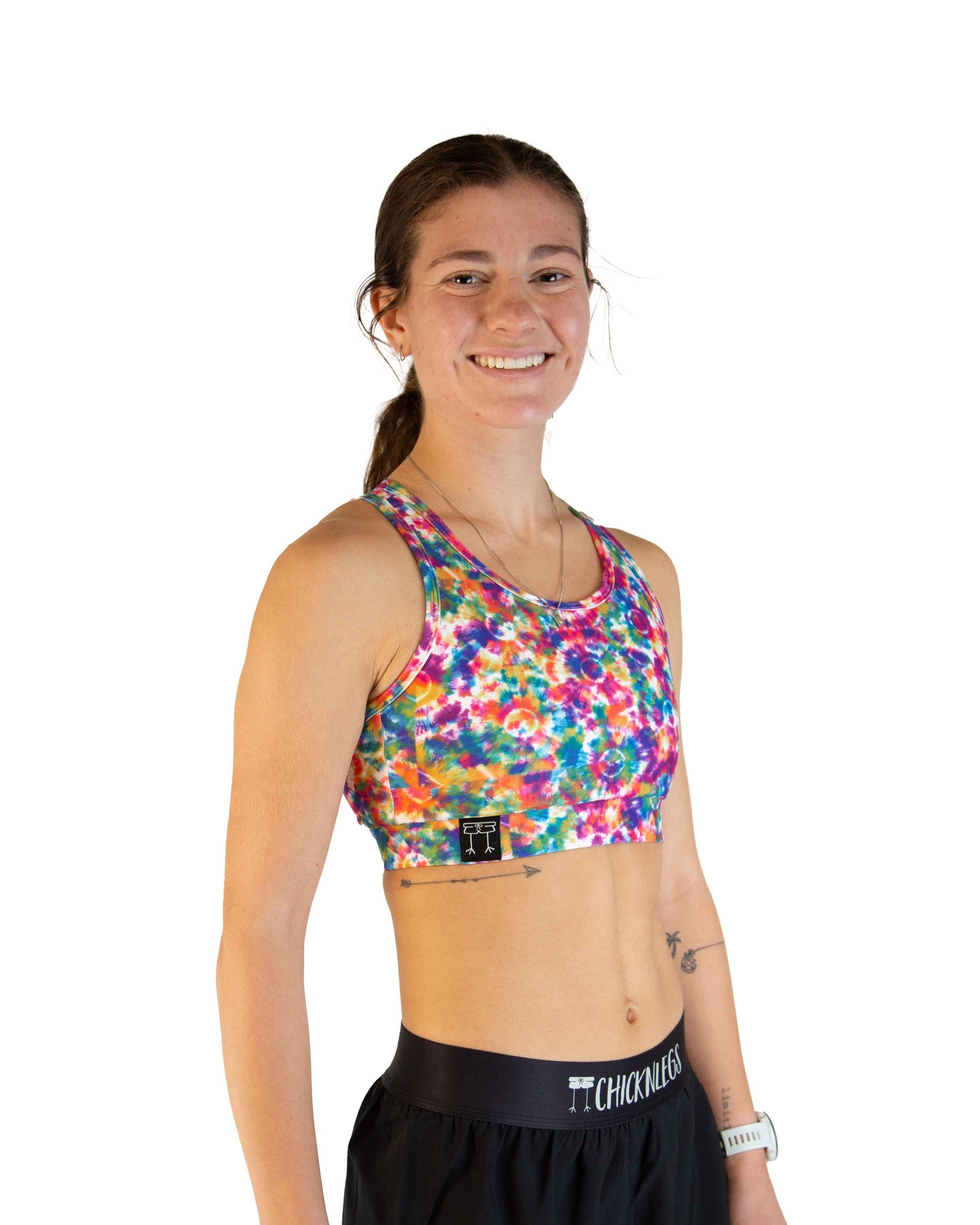 Woman wearing ChicknLegs tie-dye sports bra with colorful rainbow pattern and black shorts