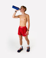Male runner wearing red ChicknLegs 2-inch DS split shorts drinking from blue water bottle