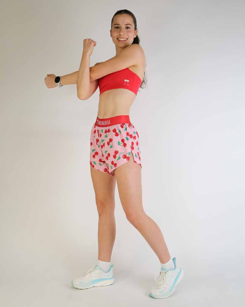 Woman modeling ChicknLegs 4-inch split running shorts in cherry print with red sports bra