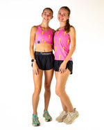 Two women wearing pink ChicknLegs sports bras with yellow lightning bolts and black shorts