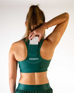 Woman wearing forest green ChicknLegs sports bra with phone pocket, back view