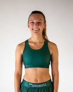 Woman wearing forest green ChicknLegs sports bra and matching shorts