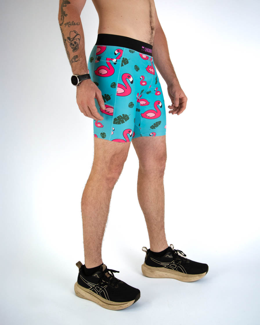 Man wearing turquoise blue shorts with pink flamingo pattern and tropical leaves