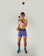 Shirtless man juggling peaches wearing blue shorts with peach print pattern