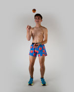 Man wearing blue shorts with red peach pattern while juggling apple