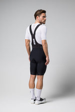 Man wearing black Gobik Limited 6.0 bib shorts with white jersey in studio