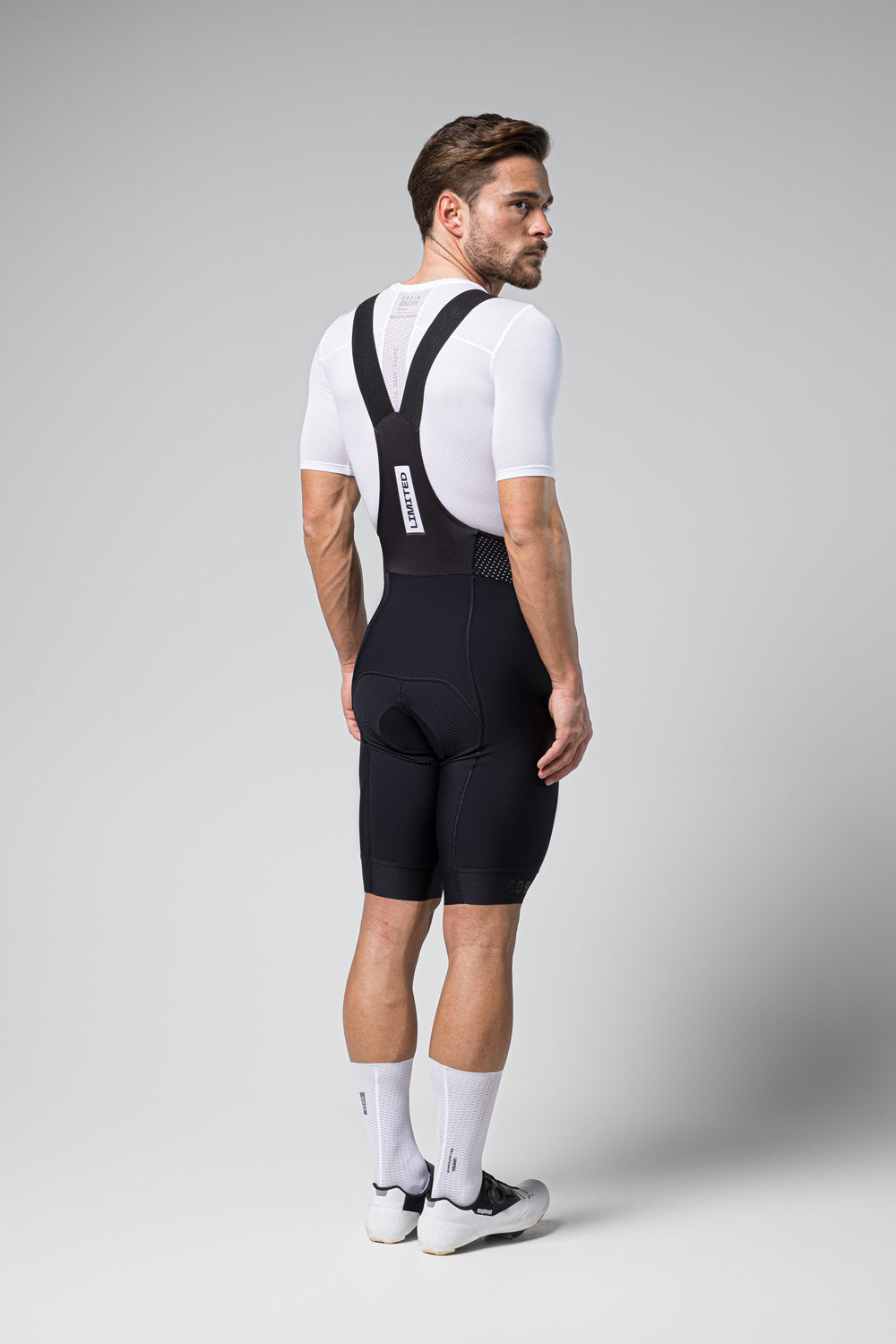 Man wearing black Gobik Limited 6.0 bib shorts with white jersey in studio