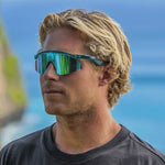 Man wearing Oakley sunglasses with translucent teal frame and green-blue mirrored lenses outdoors