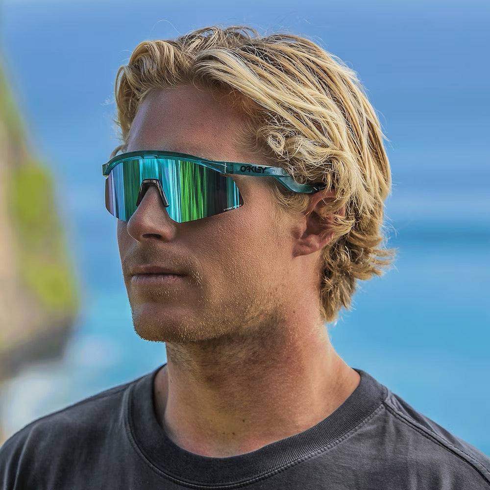 Man wearing Oakley sunglasses with translucent teal frame and green-blue mirrored lenses outdoors