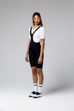 Woman wearing black Gobik Ultralite bib shorts with white jersey and cycling shoes