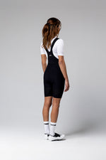 Woman wearing black Gobik Ultralite bib shorts with white top, back view