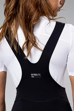 Woman wearing black Gobik Ultralite bib shorts with white jersey, rear view